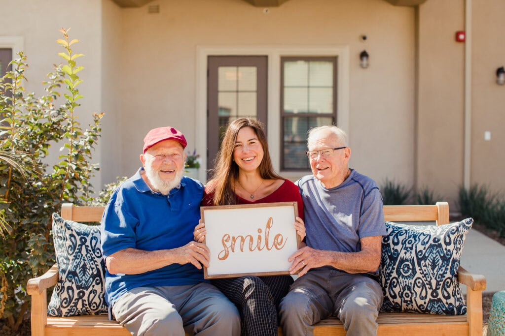 two older men with young woman holding sign that says smile