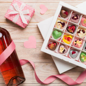 Bottle of red wine on colored background for Valentine Day with gift and chocolate. Heart shaped with gift box of chocolates top view with copy space.