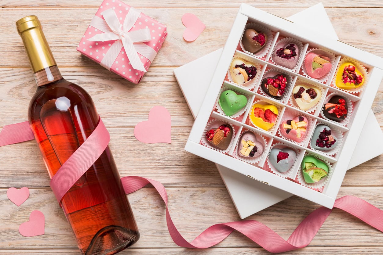 Bottle of red wine on colored background for Valentine Day with gift and chocolate. Heart shaped with gift box of chocolates top view with copy space.